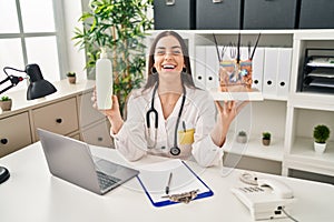 Hispanic doctor woman holding model of human anatomical skin and hair smiling and laughing hard out loud because funny crazy joke photo