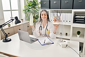 Hispanic doctor woman holding model of human anatomical skin and hair smiling looking to the side and staring away thinking photo