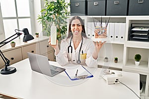 Hispanic doctor woman holding model of human anatomical skin and hair sticking tongue out happy with funny expression photo