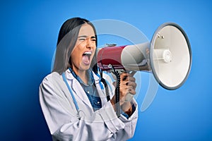 Hispanic doctor woman wearing medical white coat shouting angry on protest through megaphone