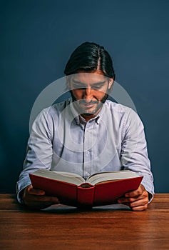Hispanic Elegant Good Man with Beard Reading Red Book Sitting on a Wooden Table Concentrared Study