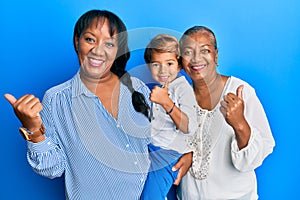 Hispanic family of grandmother, mother and son hugging together pointing thumb up to the side smiling happy with open mouth