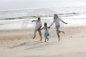 Hispanic family holding hands skipping on beach