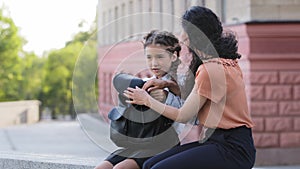 Hispanic family little cute girl daughter child schoolgirl with mom mommy sitting outdoors talking conversation