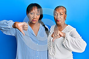 Hispanic family of mother and daughter hugging together with love with angry face, negative sign showing dislike with thumbs down,