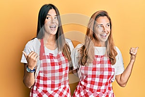 Hispanic family of mother and daughter wearing baker uniform over yellow background pointing thumb up to the side smiling happy