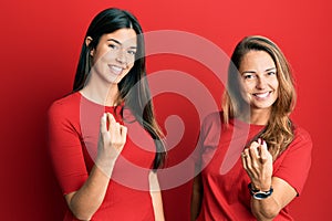 Hispanic family of mother and daughter wearing casual clothes over red background beckoning come here gesture with hand inviting