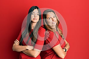 Hispanic family of mother and daughter wearing casual clothes over red background looking to the side with arms crossed convinced