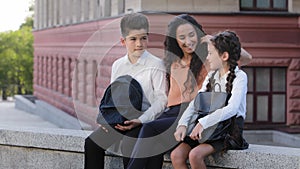 Hispanic family woman mother mommy teacher sitting outdoors on background of school building with two little children