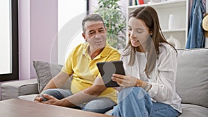 Hispanic father and daughter share a joyful, comfortable moment using a touchpad device on the roomy sofa, enhancing their