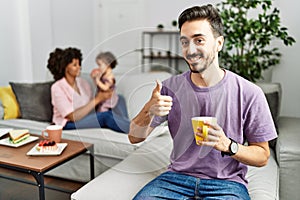 Hispanic father of interracial family drinking a cup coffee doing happy thumbs up gesture with hand