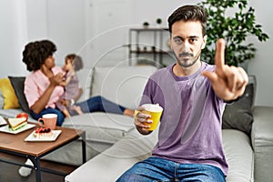 Hispanic father of interracial family drinking a cup coffee pointing with finger up and angry expression, showing no gesture