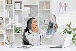 Hispanic female doctor analyzing X-ray in modern office