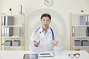 Hispanic female doctor looking at the camera says diagnose while sitting at a table in a clinic office