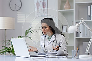 Hispanic female doctor working on a laptop in her office