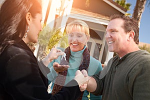 Hispanic Female Real Estate Agent Handing Over New House Keys to Happy Couple In Front of House