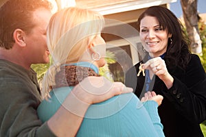 Hispanic Female Real Estate Agent Handing Over New House Keys to Happy Couple In Front of House