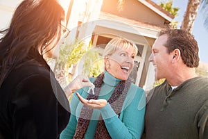 Hispanic Female Real Estate Agent Handing Over New House Keys to Happy Couple In Front of House