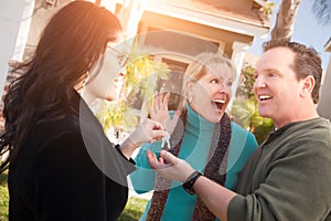 Hispanic Female Real Estate Agent Handing Over New House Keys to Happy Couple In Front of House