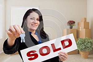 Hispanic Female Real Estate Agent with Sold Sign and Keys in Room with Moving Boxes.