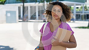 Hispanic female student with backpack and paperwork infront of university