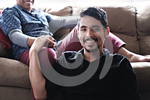 Hispanic Gay Couple Holding Hands On Sofa at Home