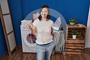 Hispanic girl with down syndrome ironing clothes at home winking looking at the camera with sexy expression, cheerful and happy