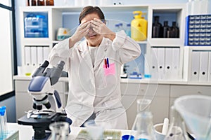 Hispanic girl with down syndrome working at scientist laboratory covering eyes with hands smiling cheerful and funny