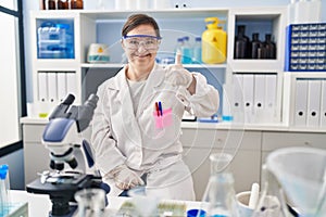 Hispanic girl with down syndrome working at scientist laboratory doing happy thumbs up gesture with hand