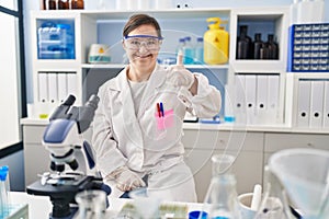 Hispanic girl with down syndrome working at scientist laboratory doing happy thumbs up gesture with hand