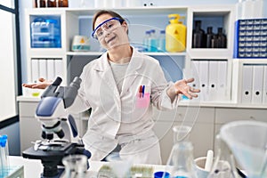 Hispanic girl with down syndrome working at scientist laboratory smiling cheerful with open arms as friendly welcome, positive and