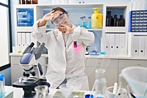 Hispanic girl with down syndrome working at scientist laboratory smiling cheerful playing peek a boo with hands showing face