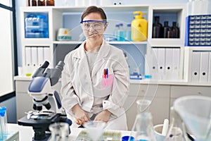 Hispanic girl with down syndrome working at scientist laboratory winking looking at the camera with sexy expression, cheerful and