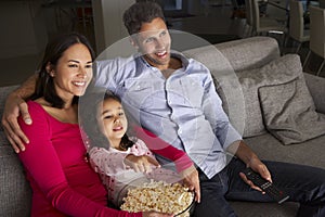 Hispanic Girl Sitting On Sofa And Watching TV With Parents