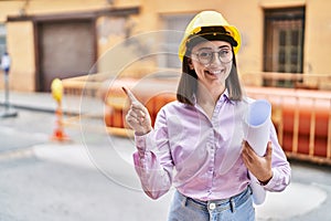 Hispanic girl wearing architect hardhat at construction site smiling happy pointing with hand and finger to the side