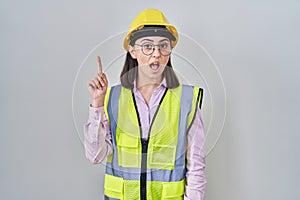 Hispanic girl wearing builder uniform and hardhat pointing finger up with successful idea