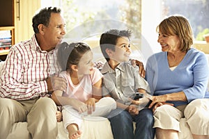 Hispanic Grandparents With Grandchildren Relaxing On Sofa At Home