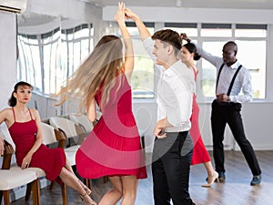 Hispanic guy practicing samba with woman in red in dance class