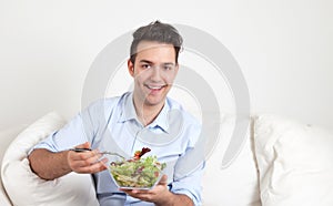 Hispanic guy sitting on sofa and eating salad