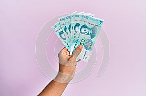 Hispanic hand holding 50 chinese yuan banknotes over isolated pink background