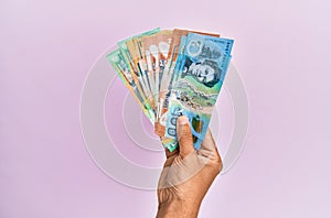 Hispanic hand holding australian dollars banknotes over isolated pink background