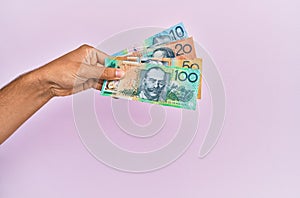 Hispanic hand holding australian dollars banknotes over isolated pink background