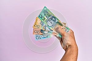 Hispanic hand holding australian dollars banknotes over isolated pink background