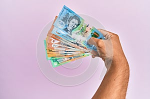 Hispanic hand holding australian dollars banknotes over isolated pink background