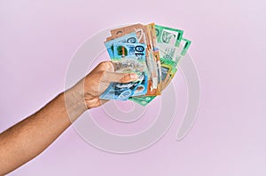 Hispanic hand holding australian dollars banknotes over isolated pink background