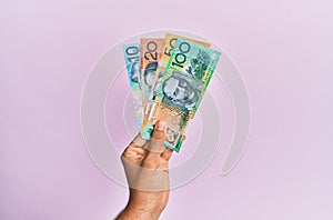Hispanic hand holding australian dollars banknotes over  pink background