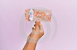 Hispanic hand holding 50 canadian dollars banknote over isolated pink background