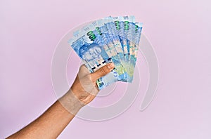 Hispanic hand holding 100 south africa rands banknotes over isolated pink background photo