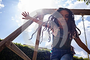 hispanic kid smiling and having fun at the park, child girl at the playground playing on a swing, action low angle shot