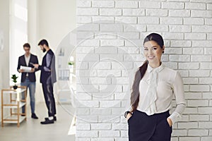 Hispanic latin business woman smiling while standing in a white office against a white wall.
